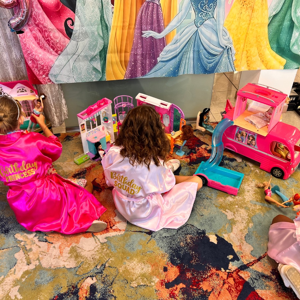 Bambine che giocano con Barbie davanti al poster Principesse Disney