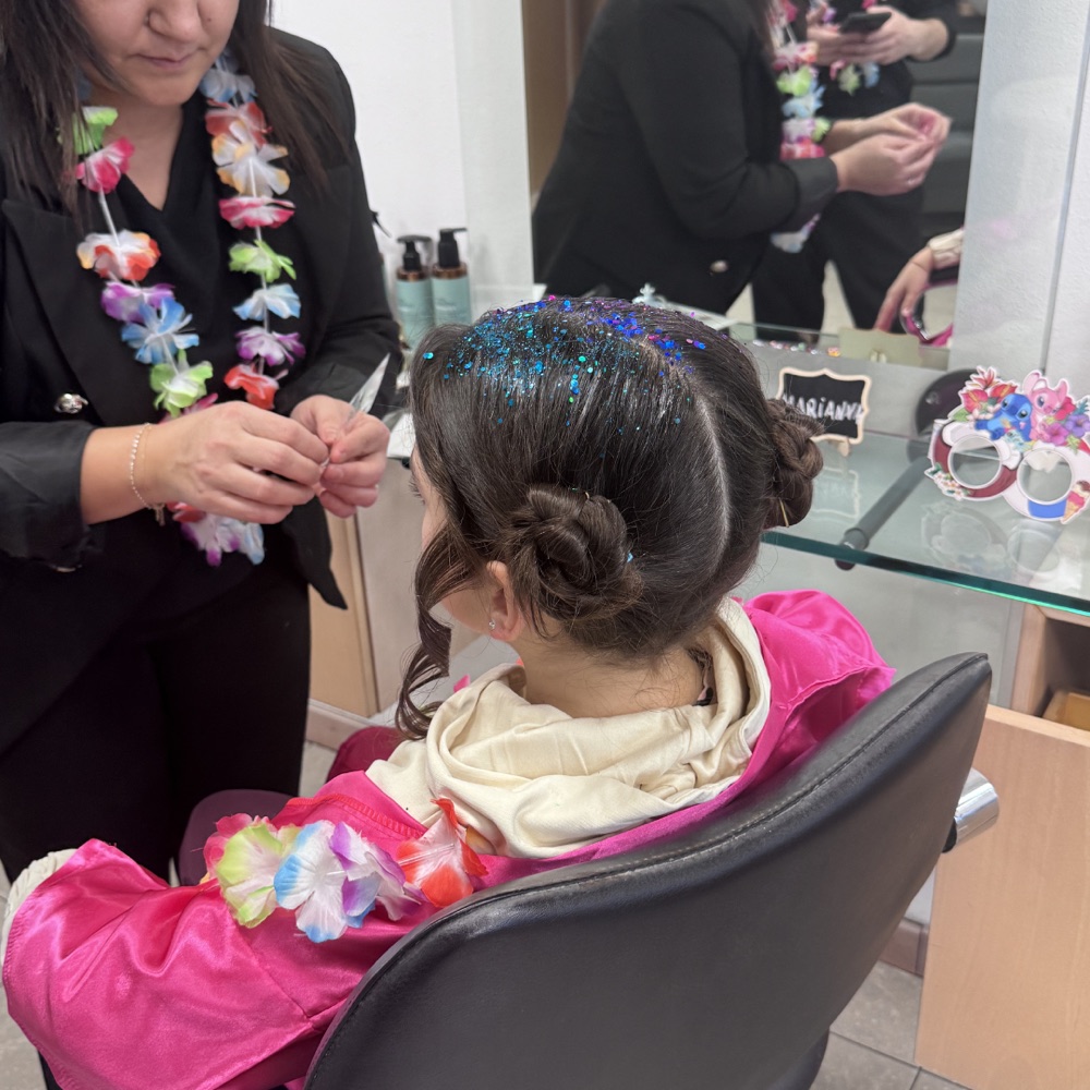 Stilista del salone acconcia una bambina con chignon e glitter colorati durante la festa principesse